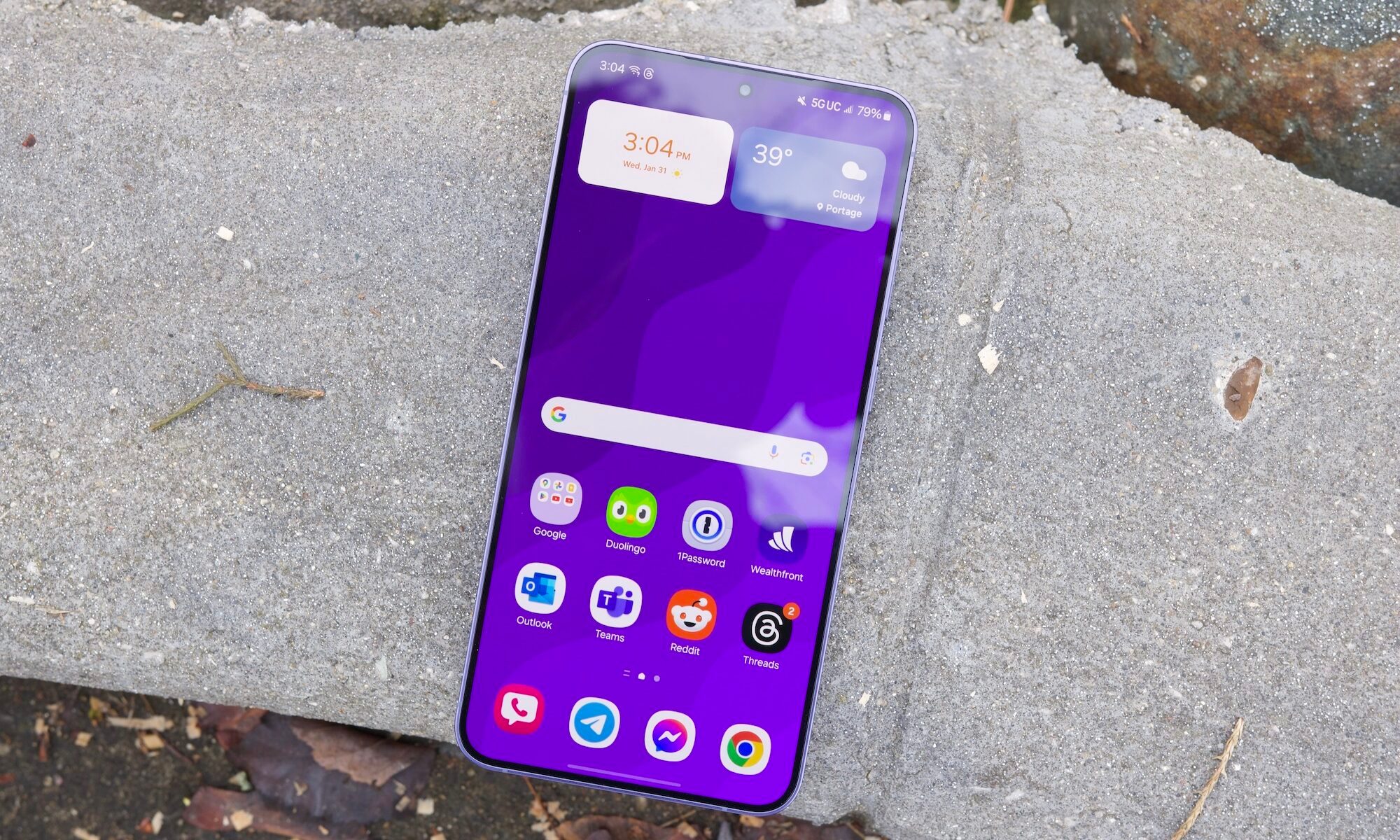 The Samsung Galaxy S24 Plus resting on a concrete slab, with the screen turned on and showing the home screen.