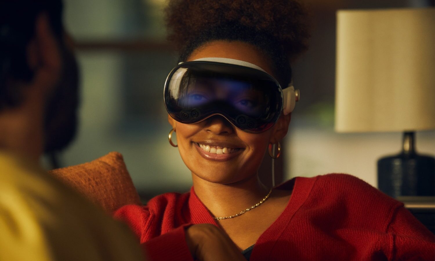 Two people talk while one wears an Apple Vision Pro headset. Their eyes are visible through the device using the EyeSight feature.