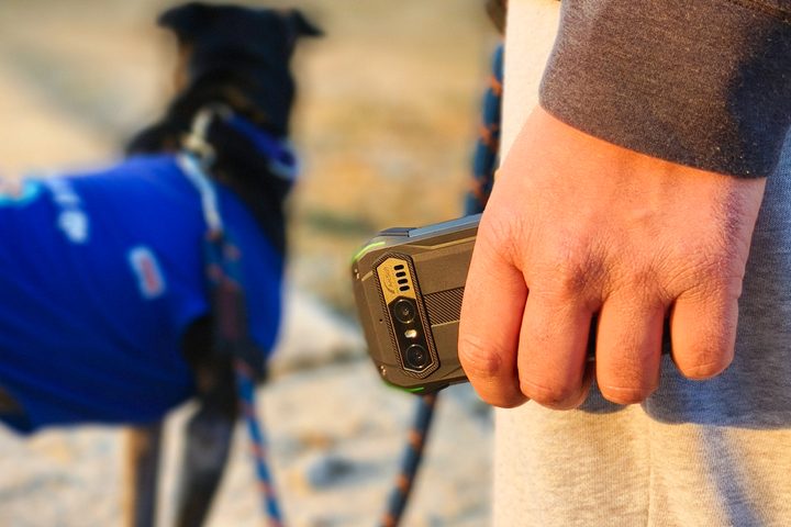 Person holding Blacview N6000 tiny rugged Android phone in hand with a black dog in a blue t shirt in the backdrop.