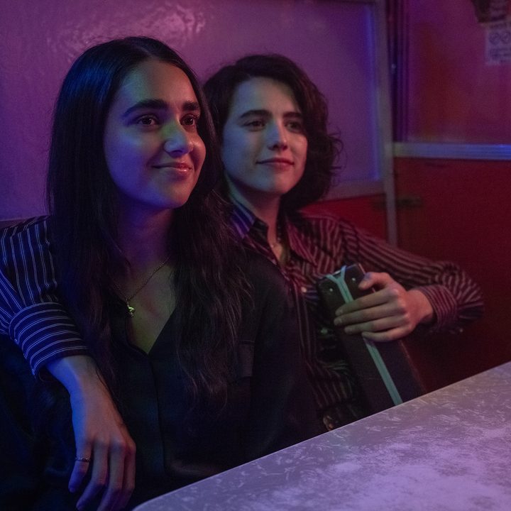 Geraldine Viswanathan and Margaret Qualley hold a briefcase and each other in a still from Drive-Away Dolls