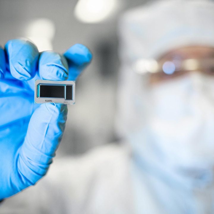 An Intel Foundry employee holds a chip between fingertips.
