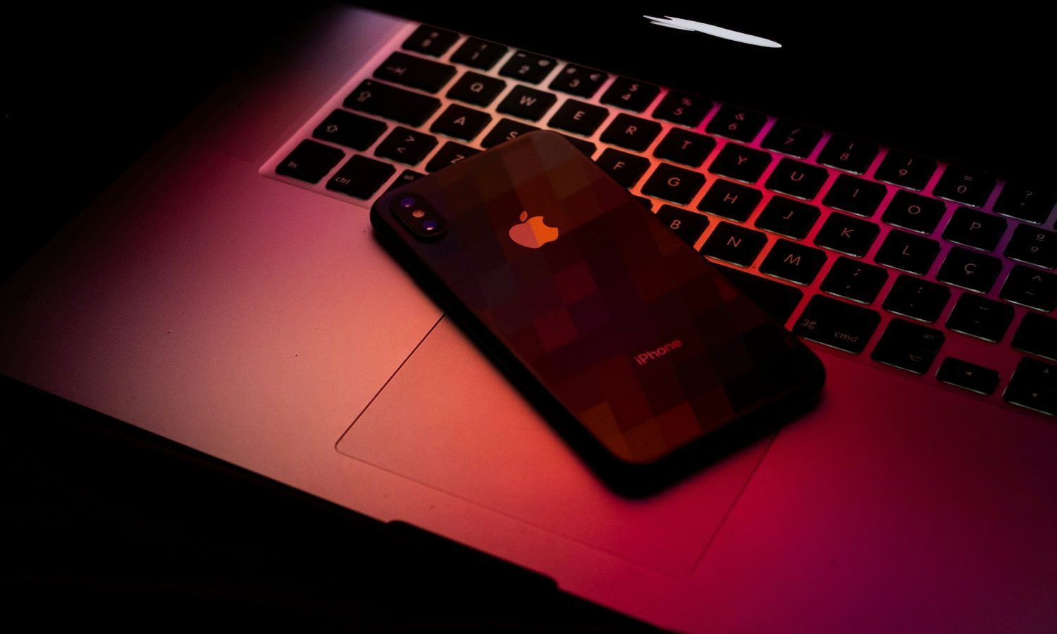 A MacBook and iPhone in dark red light.