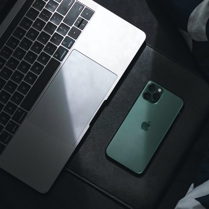 A MacBook and iPhone in shadow on a surface.