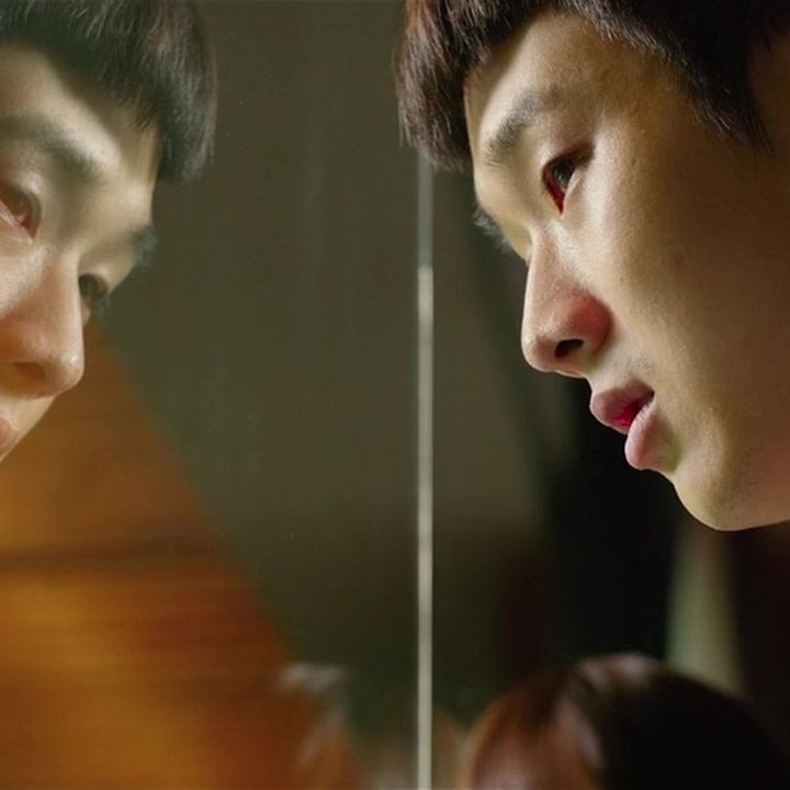 Choi Woo-shik looks out of a window longingly, his reflection staring back at him, in a still from the movie Parasite.
