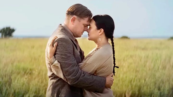 A man and a woman kiss in a field in Killers of the Flower Moon.