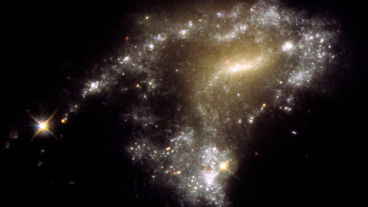 Galaxy AM 1054-325 has been distorted into an S-shape from a normal pancake-like spiral shape by the gravitational pull of a neighboring galaxy, seen in this Hubble Space Telescope image. A consequence of this is that newborn clusters of stars form along a stretched-out tidal tail for thousands of light-years, resembling a string of pearls. They form when knots of gas gravitationally collapse to create about 1 million newborn stars per cluster.