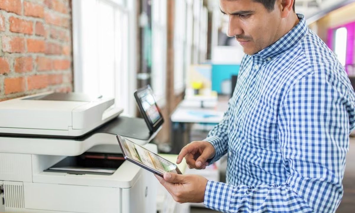 A person uses a tablet with an HP laser printer in an office.