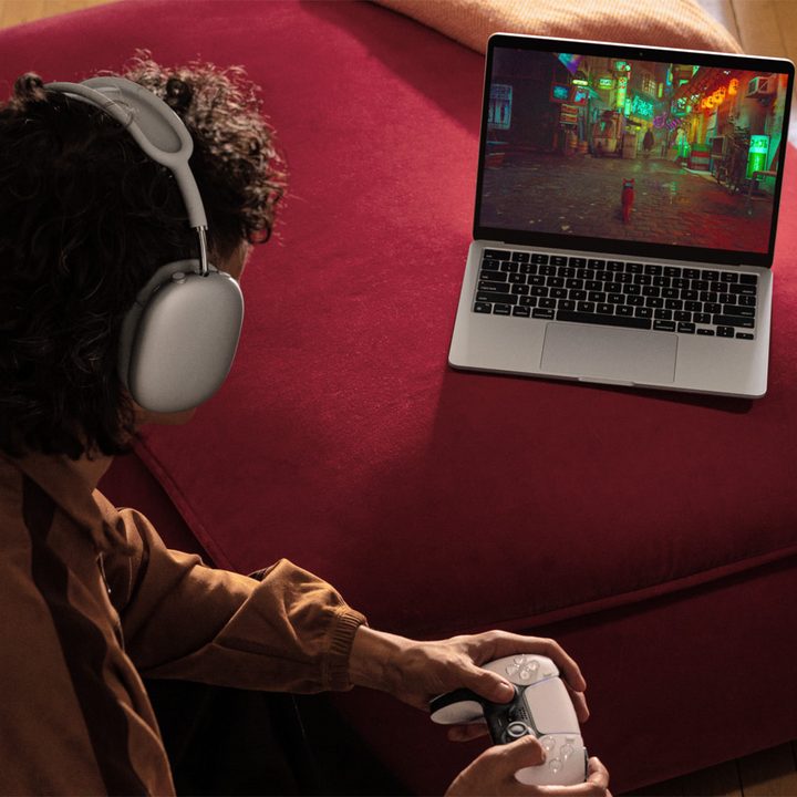 An Apple press photo of someone playing a game on a MacBook Air with a controller.