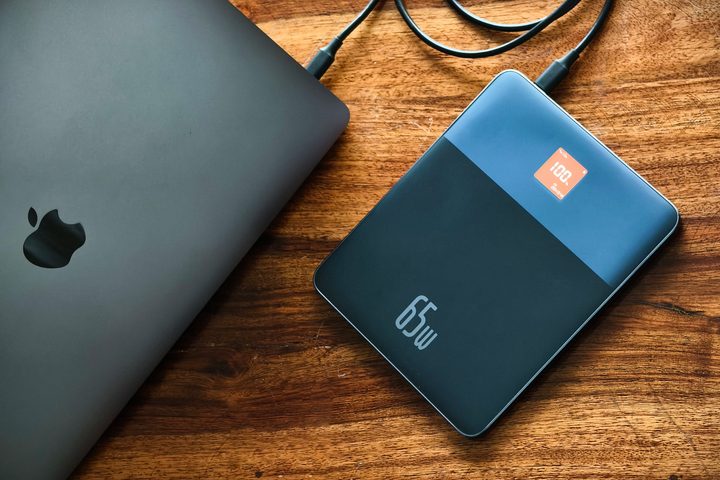 Baseus Blade 2 65W fast charging power bank for laptops kept on a table alongside a MacBook partially folded.