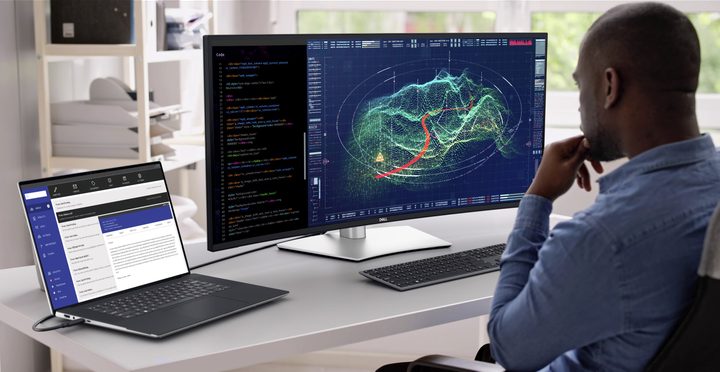 A person using the Dell UltraSharp 40 U4025QW 40-inch curved Thunderbolt hub monitor with a Dell laptop on a desk.