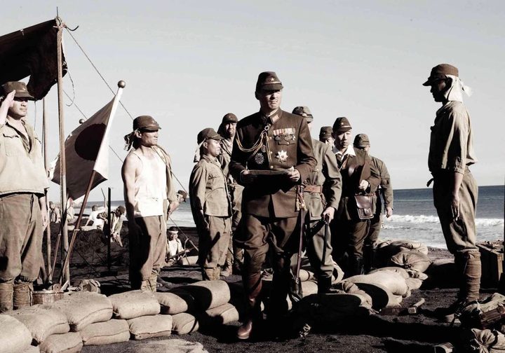 A group of Japaneze soldiers stand on a beach as one walks into a bunker.