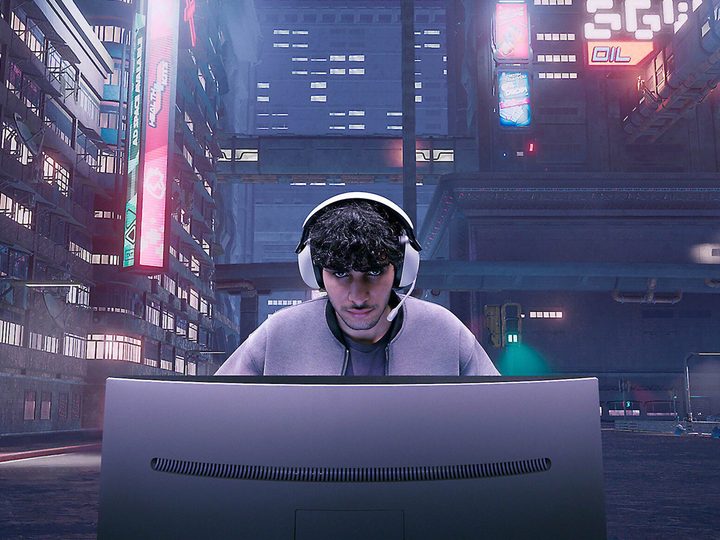 A gamer sits at a monitor wearing the Sony INZONE H9 gaming headset.