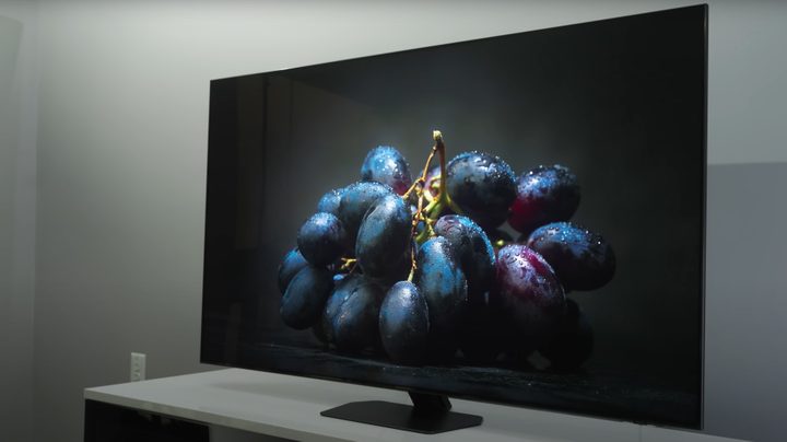 A closeup of moodily lit dark purple grapes on a black background shown on a Samsung QN90D.