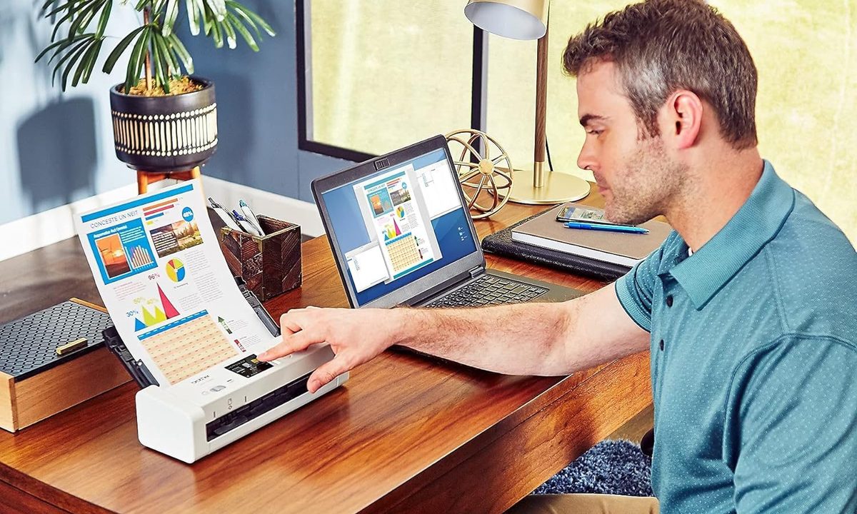 A man uses the Brother ADS-1700W to scan a colorful document on his desk.