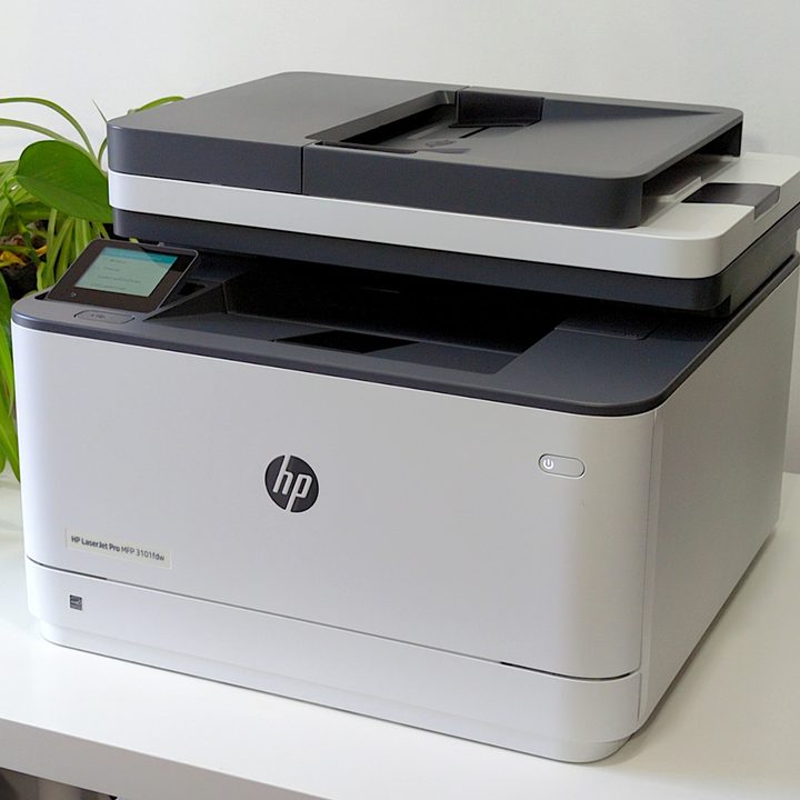HP LaserJet Pro MFP 3101fdw printer looks nice on a white stand beside plants.