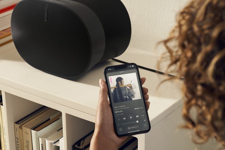 A hand-held iPhone showing the new Sonos app's now-playing screen.