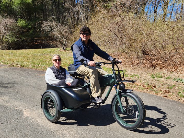 Two smiling people with shades riding a MOD Easy Sidecar3 on a private road