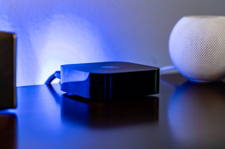 An Apple TV 4K sitting on a wood entertainment center with a HomePod Mini behind it.