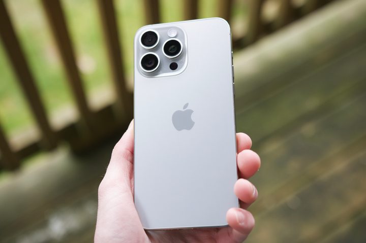 Someone holding an iPhone 15 Pro Max outside on a patio, showing the back of the Natural Titanium color.