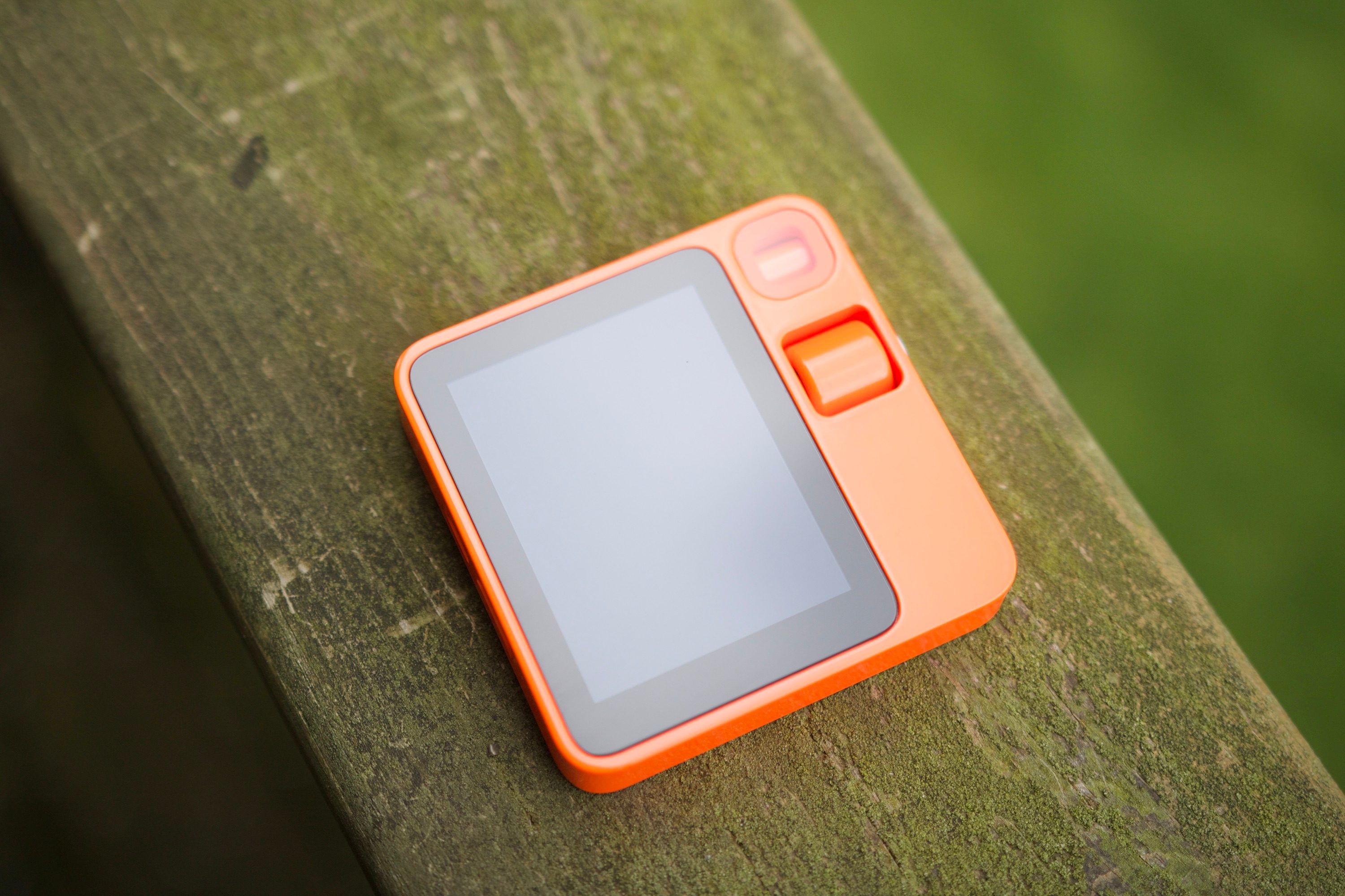 The Rabbit R1 laying on a wooden railing, showing the front of the device.
