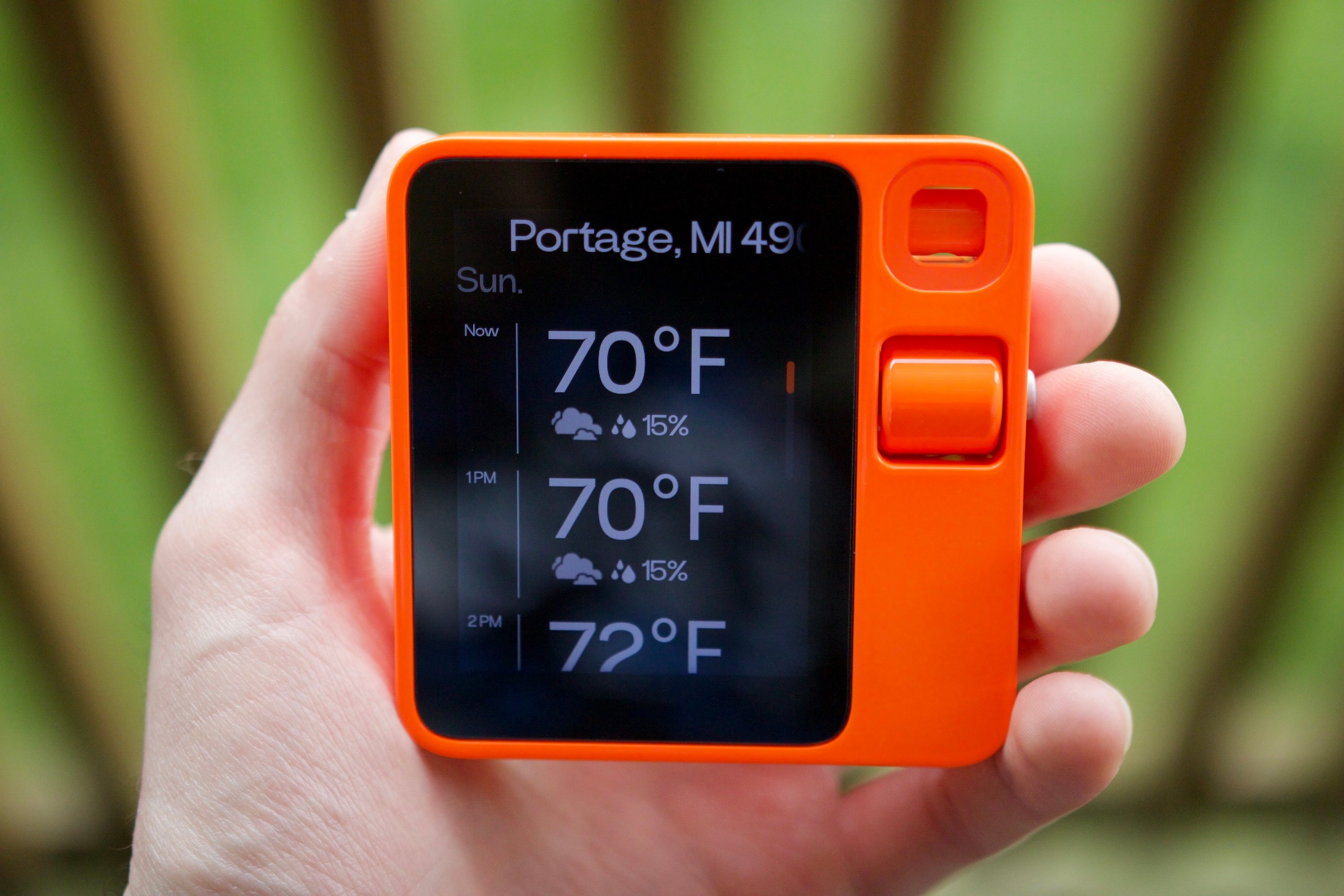 Someone holding the Rabbit R1, with the device showing the weather forecast.