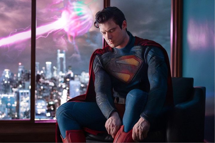 David Corenswet as Superman pulling up his red boot while wearing a costume.