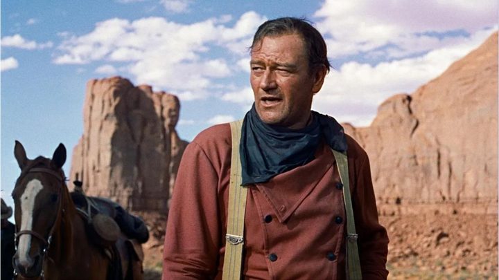 John Wayne as Ethan Edwards in the desert looking intently at something off-camera in The Searchers.