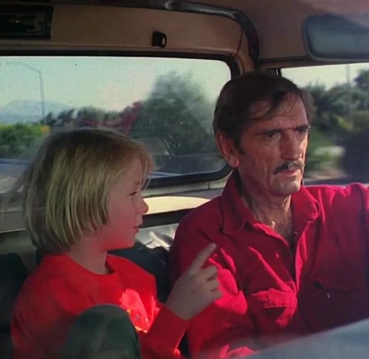 A man drives a car with a child in the passenger seat.