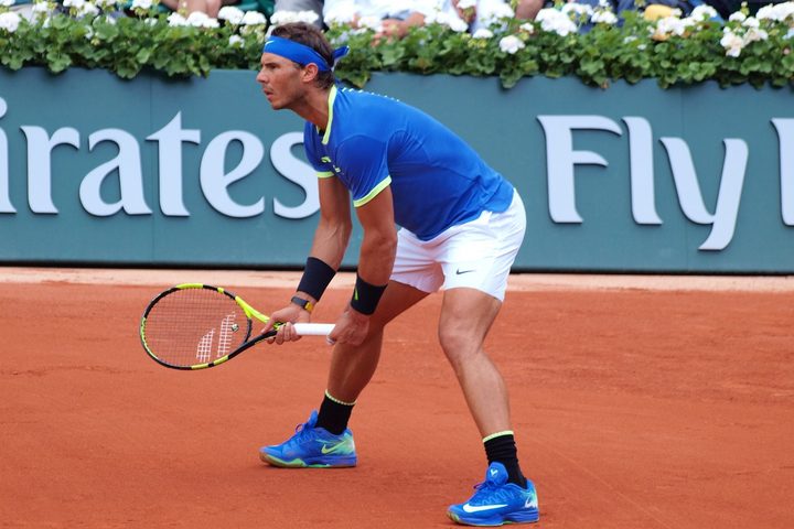 Rafael Nadal stands with his racket and prepares to hit a tennis ball.