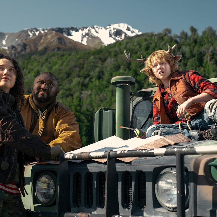 A young boy sits on a Jeep with two adults standing in front of him.