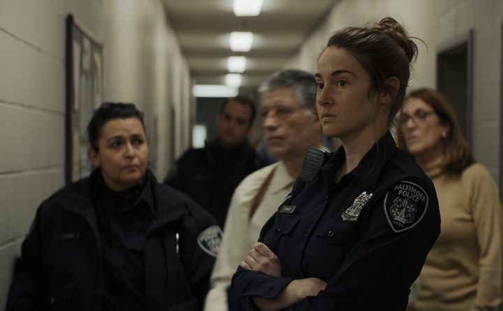 A cope stands with her arms folded in front of people.