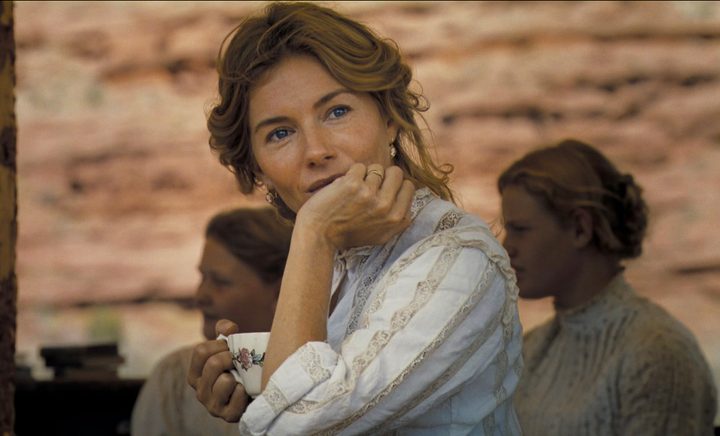 A woman tucks her hand under her chin and stares.