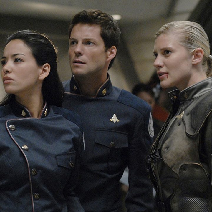 Three people standing inside a ship in a scene from Battlestar Galactica.