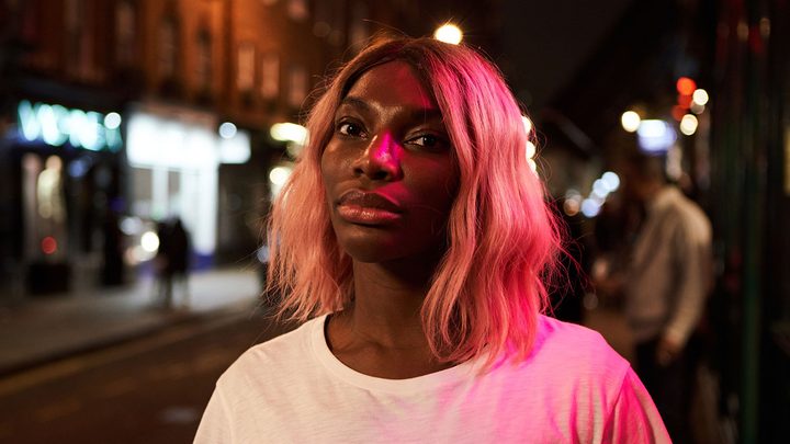 A woman stands in a dark street wearing a T-shirt and looking sad in a scene from I May Destroy You on Max.