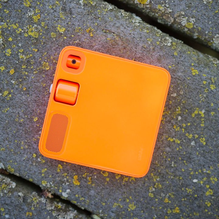 The back of the Rabbit R1, with the device laying face-down on a walkway.