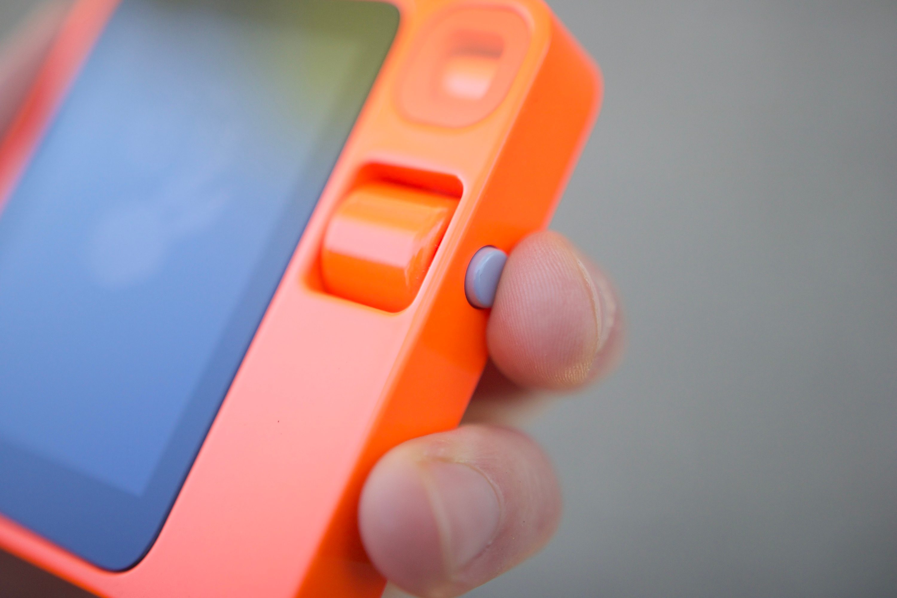 A close-up photo of someone pressing the button on the Rabbit R1.