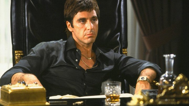 Al Pacino as Tony Montana in Scarface sitting at his desk in an iconic scene.
