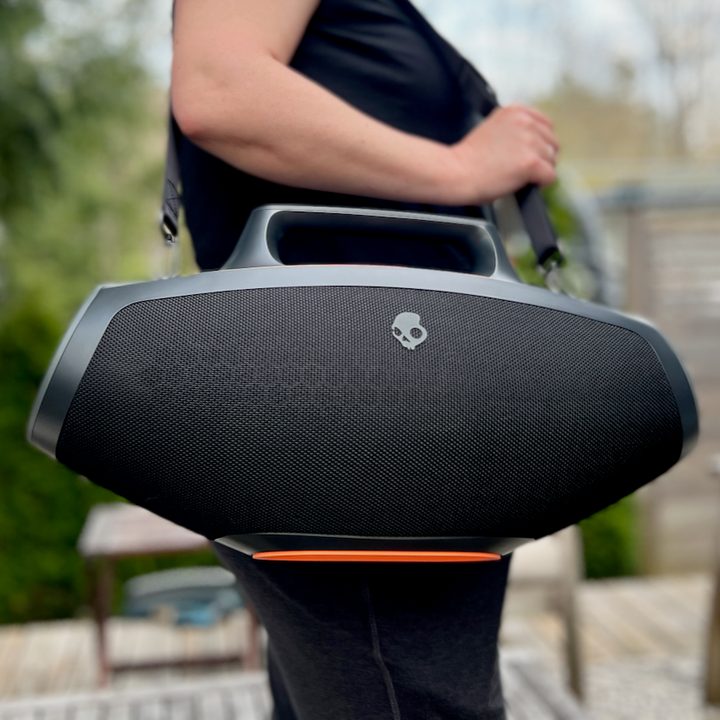 A person carrying the Skullcandy Barrel Bluetooth speaker with the shoulder strap.