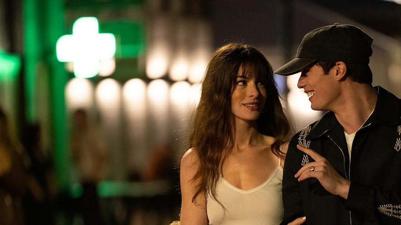 A woman and man link arms and stare into each other's eyes while walking outside at night in a scene from The Idea of You.