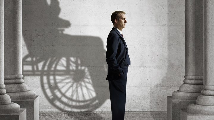 A man standing in a suit facing the right, a silhouette of a person in a wheelchair behind him from the miniseries The World Wars.