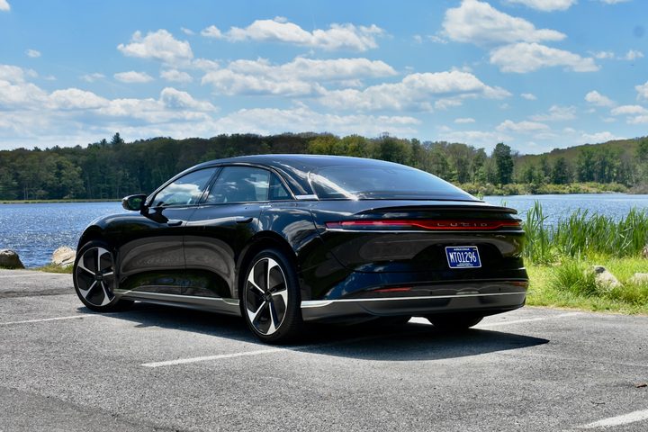 Rear three quarter view of a black 2024 Lucid Air Pure in front of a lake.