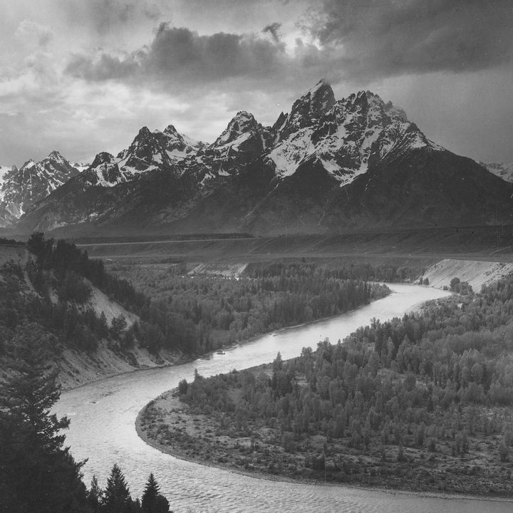Ansel Adams' panorama of Grand Teton National Park with the peak in the background and a meandering river in the forest.