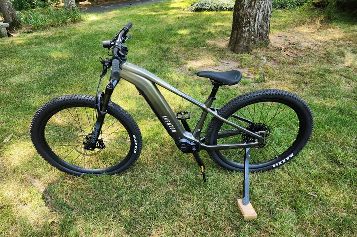 Aventon Ramblas eMTB left profile shot with grass, bushes, and trees in the background.