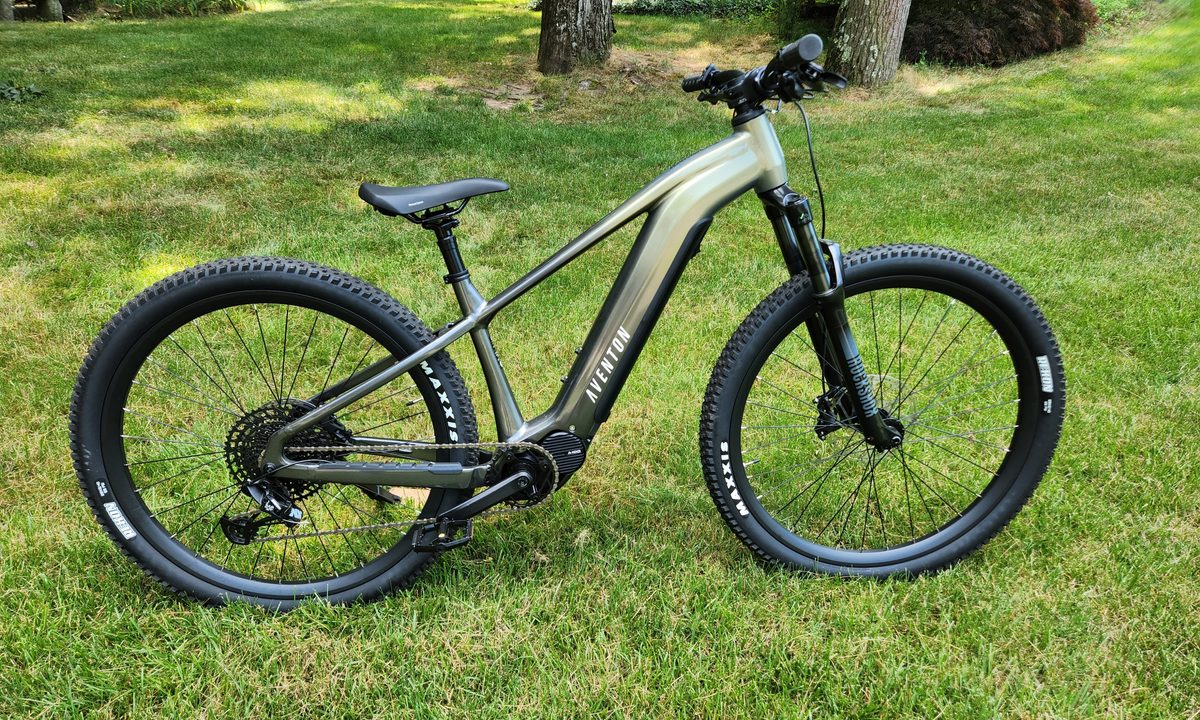 Aventon Ramblas eMTB right profile with grass, bushes, and trees in the background