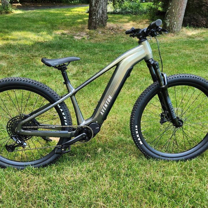 Aventon Ramblas eMTB right profile with grass, bushes, and trees in the background