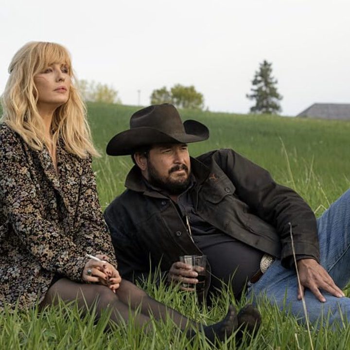 A woman sits down next to a man lying down on a hill.