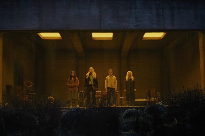 Four people stand in a viewing room in The Watchers.