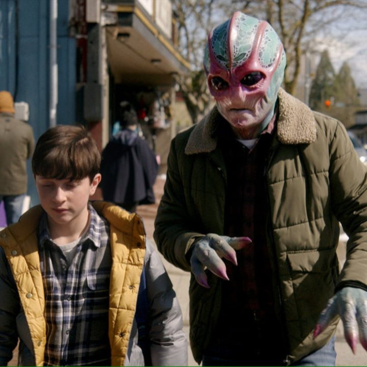 An alien walks with a boy down the street.