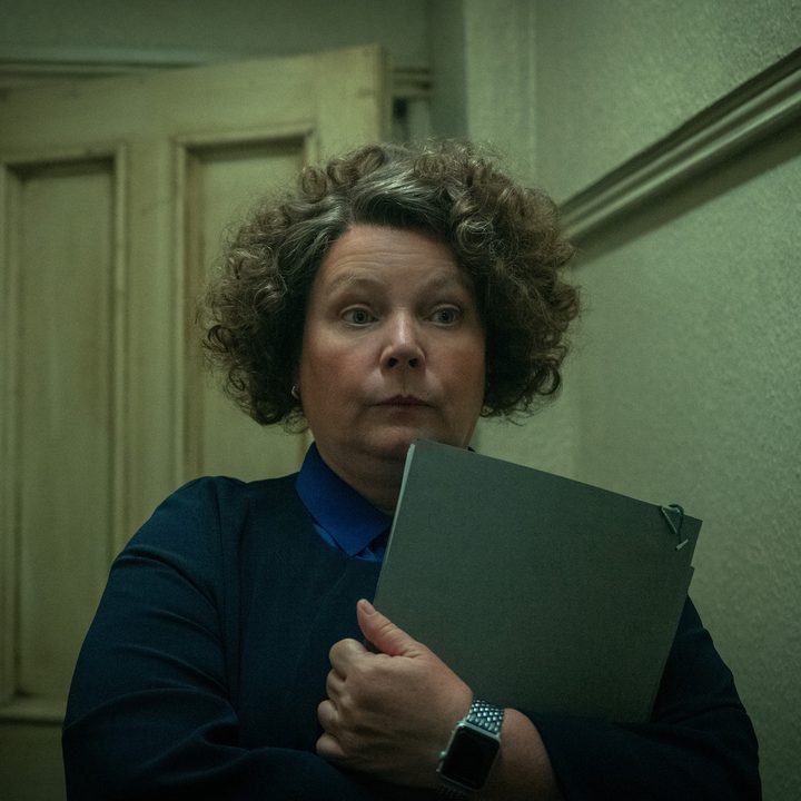 A woman holds a notebook in a hallway.