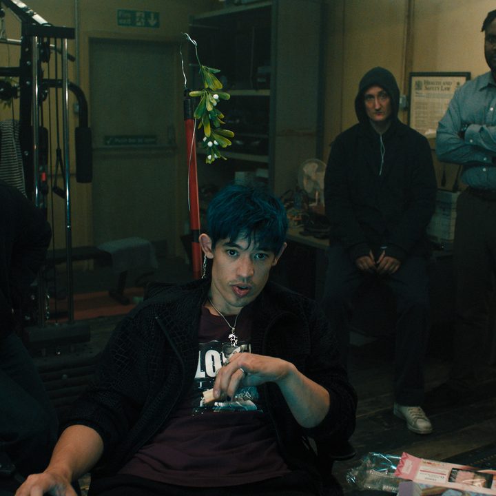 A man sits down as other people stand over his shoulder.